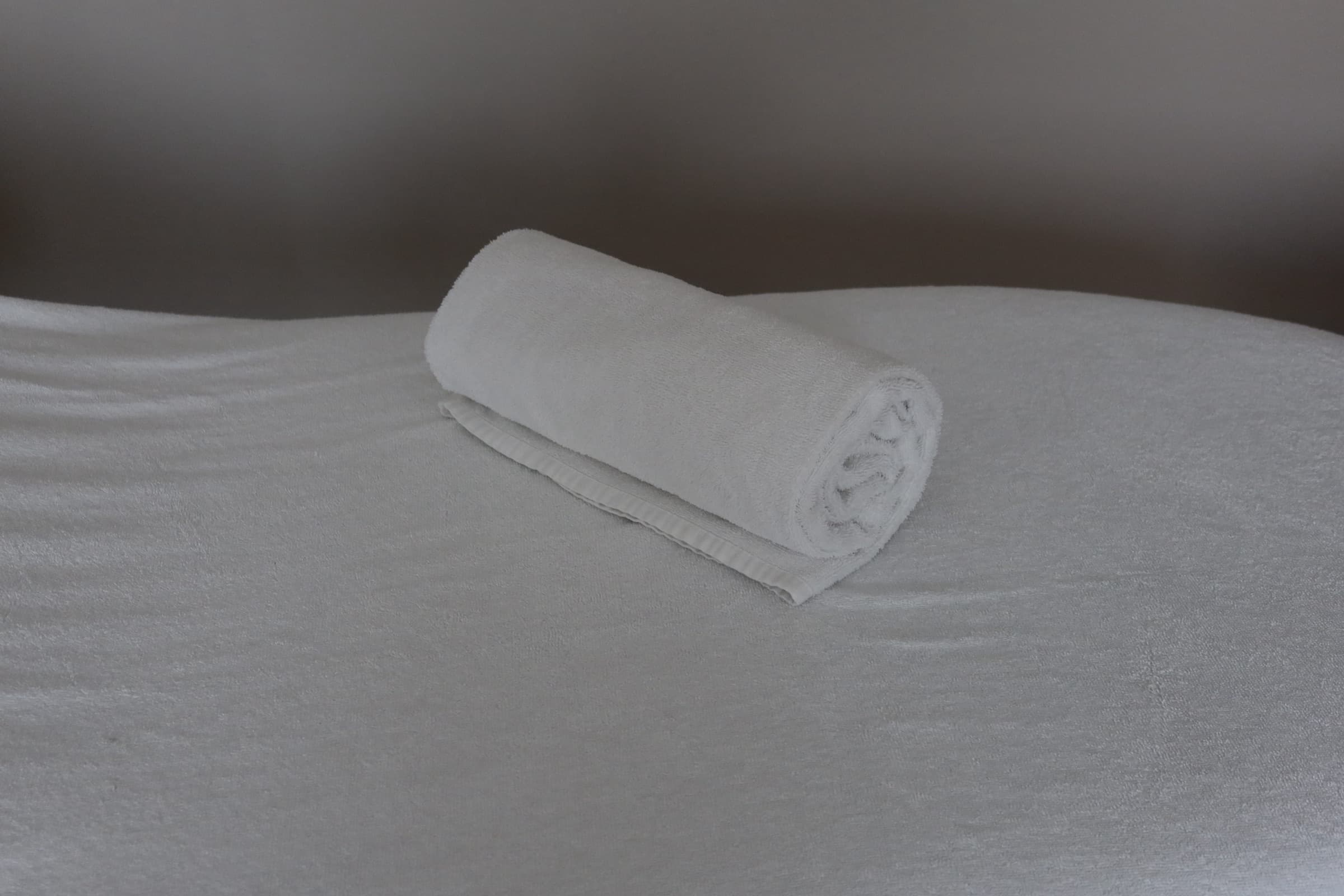 A made massage table in the treatment room, with a rolled white towel laid across the crisp white cover.